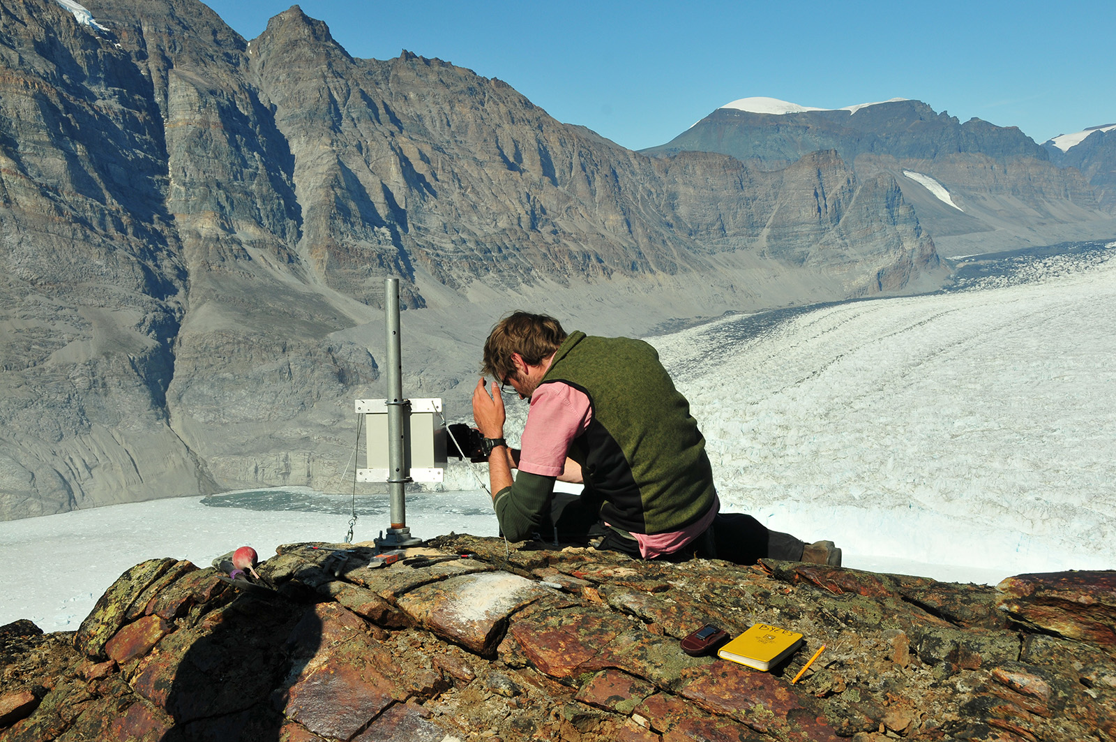 "Researcher on top of a hill surrounded by snow capped mountains"